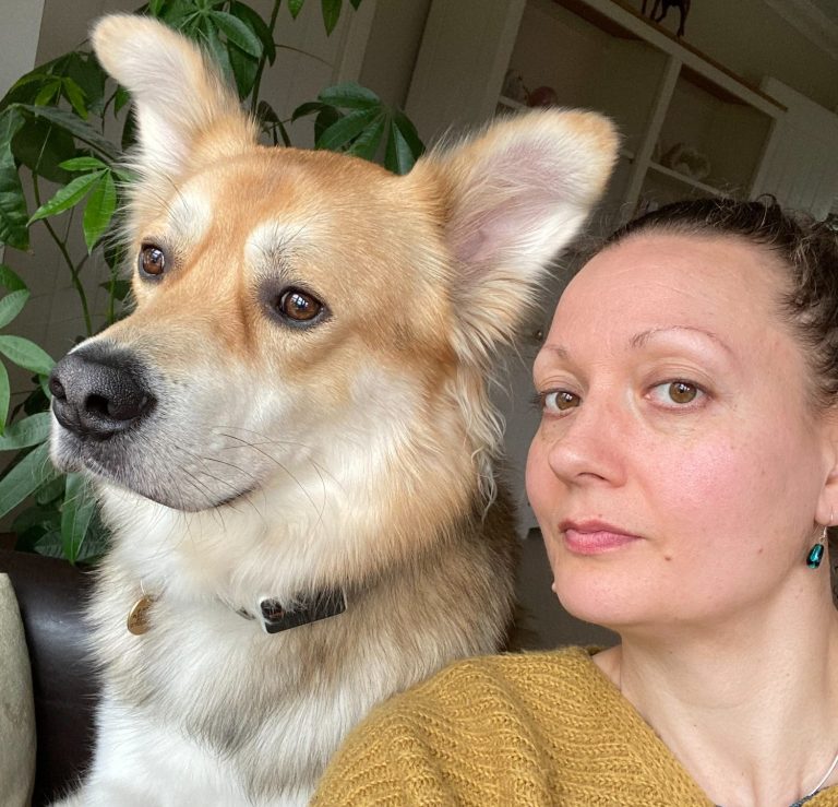 A person with medium-length hair sits beside a light-coloured dog.